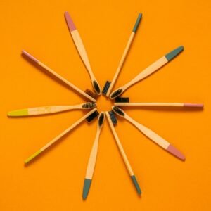 Colorful bamboo toothbrushes arranged on a bright orange background, promoting eco-friendly oral care.