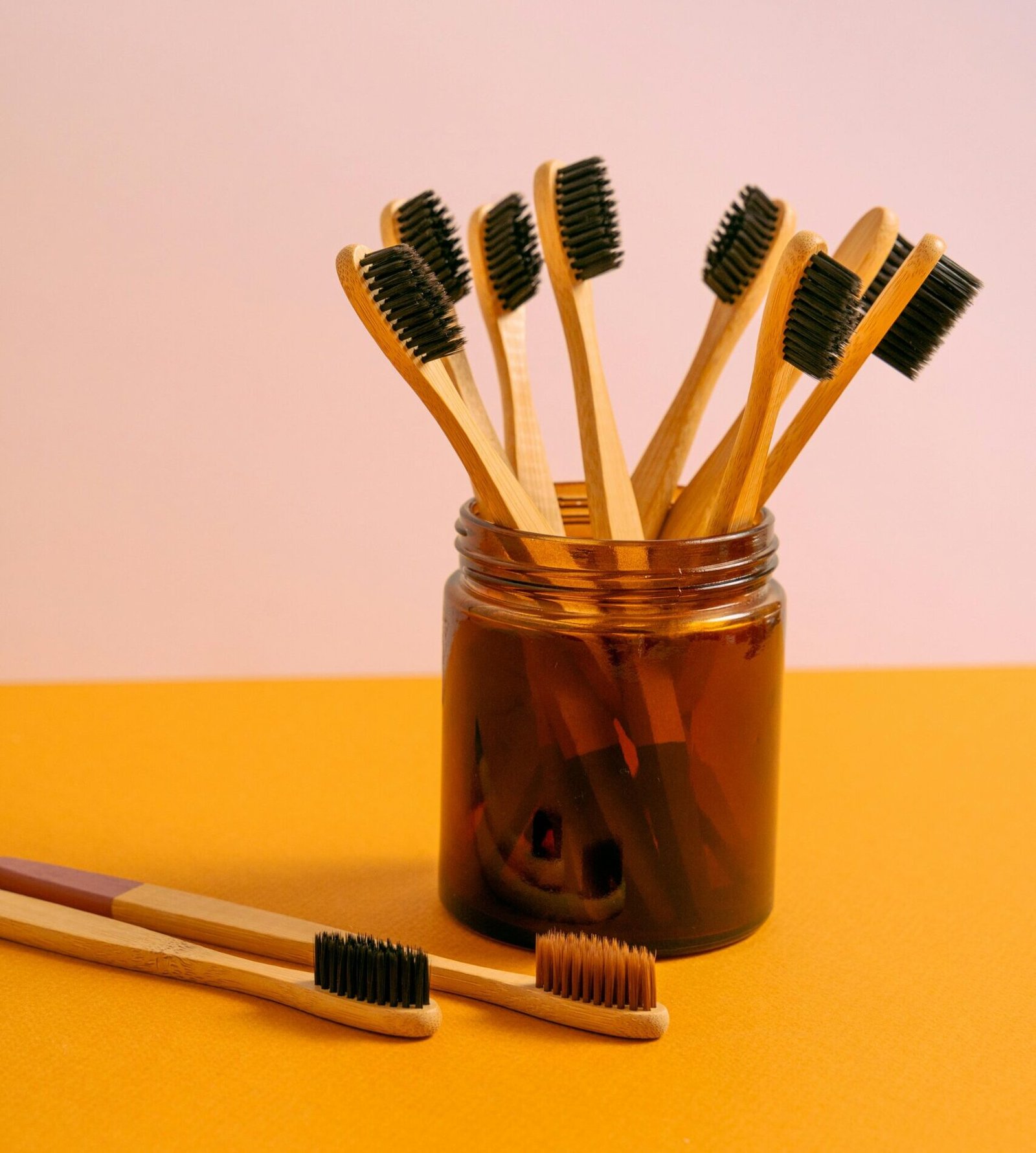 Stylish arrangement of bamboo toothbrushes in a glass jar on an orange surface, eco-friendly oral care.